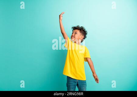 Porträt eines optimistischen kleinen Jungen mit lockigen Haaren Tragen Sie ein stilvolles T-Shirt, das auf einem türkisfarbenen Hintergrund isoliert ist Stockfoto