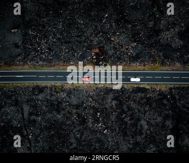Straße mit zwei Autos mit Bewegungsunschärfe von oben durch Drohne - Nachtfoto auf Lanzarote. Gerade Straße zwischen den Lavas auf den Kanarischen Inseln Stockfoto