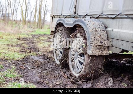 Zweiachsiger Anhänger mit schlammigen Rädern auf einer matschigen Straße im Herbst. Transport von Gütern auf einer schlechten Straße. Stockfoto