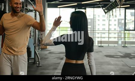 Rückansicht Sportlerin Fitnesstrainer gehen durch Sportgeräte im Fitnessstudio nach dem Workout unbekannte schlanke Passform Frau trifft Mann Sportler geben hohe fünf Respekt Stockfoto