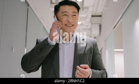 Asiatischer Geschäftsmann mittleren Alters Erwachsener Unternehmer im Büro Flur sprechen Mobiltelefon verhandeln per Smartphone lächelnder chinesischer koreanischer japanischer Mann Stockfoto