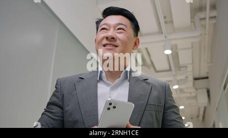 Asiatischer Mann mittleren Alters Geschäftsmann Unternehmer verwenden Telefon Handy moderne Technologie gewinnen Geschäftsgelegenheit bieten glücklichen chinesischen koreanischen Unternehmer Stockfoto