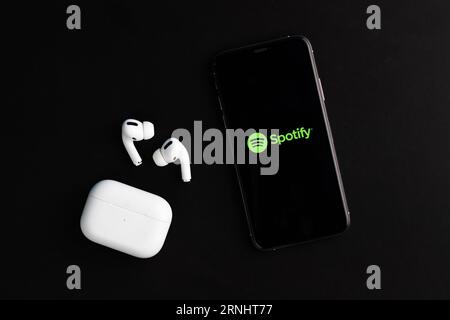 Spotify Logo auf dem Telefonbildschirm mit Airpods Pro auf dem Schreibtisch Stockfoto