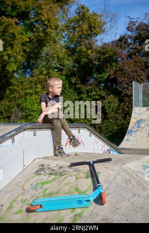 Boy on Scooter macht einen Trick und genießt seine Fahrt im Skatepark am bewölkten Frühlingstag. Junger Mann macht Trick auf dem Tretroller im Park. Fu Stockfoto