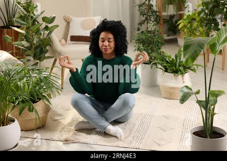 Entspannende Atmosphäre. Frau meditiert in der Nähe von Zimmerpflanzen im Zimmer Stockfoto