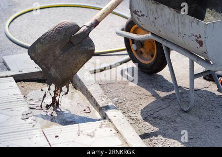 Arbeiter legt Grundsteine des Hauses. Ansicht der Schaufel mit Flüssigzement. Baustellenreparatur am Sommertag draußen. Stockfoto