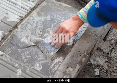 Ziegelsteinleger legen Pflasterplatten an einem Sommertag. Nahaufnahme der Hand eines Bauherren von oben. Reparatur des Gehwegs. Stockfoto