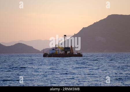 Plattform auf See mit Kran und Hügeln im Hintergrund. Stockfoto