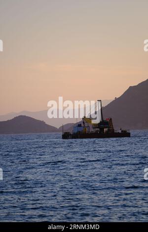 Plattform auf See mit Kran und Hügeln im Hintergrund. Stockfoto