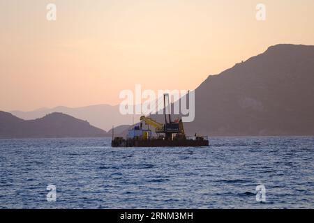 Plattform auf See mit Kran und Hügeln im Hintergrund. Stockfoto