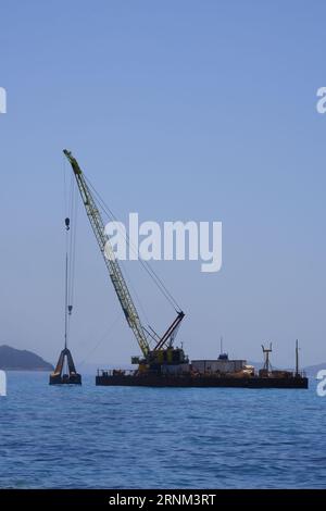 Plattform auf See mit Kran und Hügeln im Hintergrund. Stockfoto