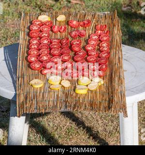 Halb rote Tomaten werden auf einem Tisch in der Sonne zum Trocknen aufgestellt, mit Apfelscheiben daneben Stockfoto