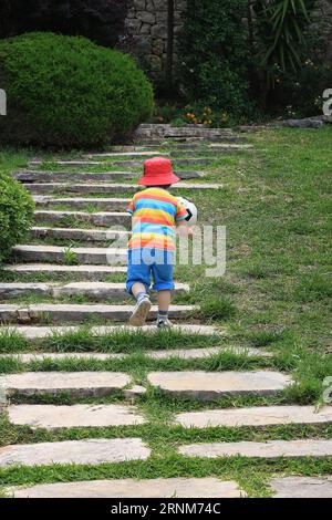 Ein Kleinkind, das eine Treppe im Freien trägt und einen Fußball in den Händen hält. Stockfoto