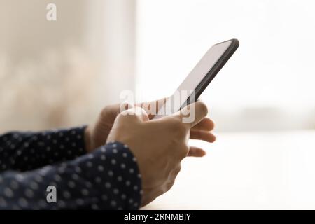 Seitenansicht des dunklen Smartphones in weiblichen Händen auf dem Tisch Stockfoto