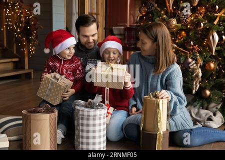 Glückliche kleine Kinder öffnen Weihnachtsgeschenke mit Eltern. Stockfoto