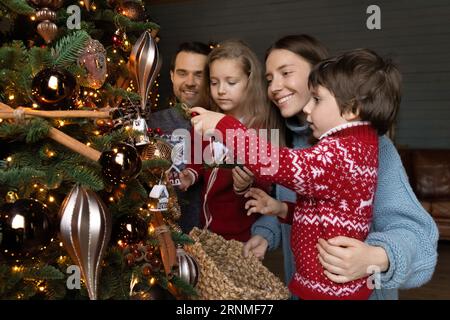 Glückliche Eltern, die Weihnachtsbaum mit kleinen Kindern dekorieren. Stockfoto