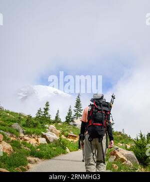 Man Hiking Skyline Loop Trail im Sommer im Mount Rainier National Park. Der Berg Rainier blickt durch die Wolken. Washington State. Vertikales Format. Stockfoto