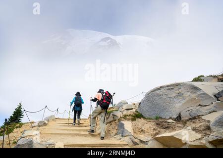 Zwei Personen wandern im Sommer auf dem Skyline Loop Trail im Mount Rainier National Park. Der Berg Rainier blickt durch die Wolken. Washington State. Stockfoto