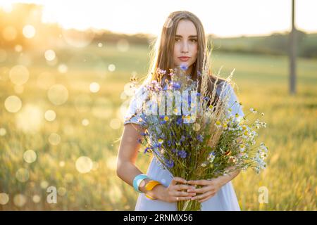 Junge Frau auf einem Weizenfeld mit einem Blumenstrauß von Gänseblümchen und Kornblumen Stockfoto