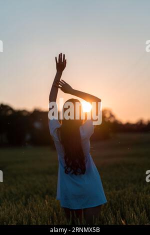 Ein schlankes junges Mädchen in einem kurzen Kleid steht im Weizen und blickt auf die untergehende Sonne Stockfoto