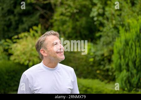 Ein Mann mittleren Alters schaut mit einem fröhlichen Lächeln in den Himmel, während er im Garten steht Stockfoto
