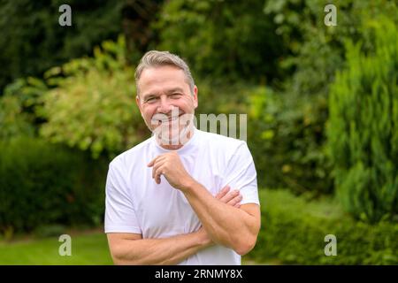Attraktiver Mann mittleren Alters in seinen 50ern lächelt glücklich vor der Kamera, während er im Garten steht Stockfoto