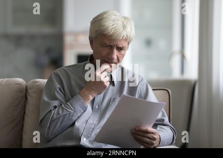 Ernsthaft besorgt, älterer pensionierter Mann, der ein Dokument liest, einen Brief Stockfoto