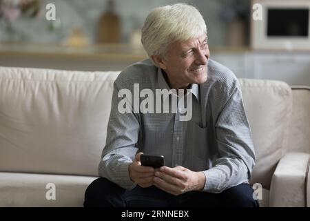 Glücklicher älterer Reifer, der ein Handy hält und auf dem Sofa sitzt Stockfoto