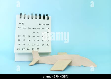 Selektiver Fokus auf November 2023 Tischkalender auf blauem Hintergrund mit Holzflugzeugmodell. Thanksgiving Tagesreise und Urlaubskonzept. Stockfoto