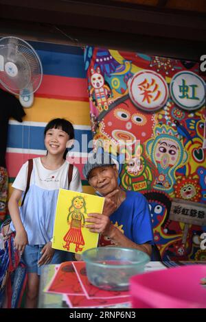 (170813) -- TAICHUNG, 13. August 2017 -- Huang Yong-Fu posiert für ein Foto mit einem Touristen in einer Wohnsiedlung namens Rainbow Village im Nantun Bezirk von Taichung City, Südostchinas Taiwan, 12. August 2017. Huang Yong-Fu, ein 95-jähriger Veteran, malte vor einigen Jahren farbenfrohe Tiere und Figuren auf die Wände und das Gelände des Dorfes. Seine Gemälde zogen viele Touristen an und retteten auch das sterbende Dorf vor der Entfernung. Er steht jeden Tag um 3 Uhr morgens auf, um die Gemälde seines Dorfes zu reparieren. ) (Zkr)(zt) CHINA-TAICHUNG- RAINBOW VILLAGE (CN) ZhouxMi PUBLICATIONxNOTxINxCHN Stockfoto