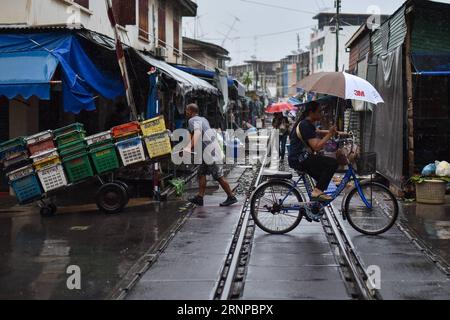 (170821) -- MAEKLONG, 21. Aug. 2017 -- Ein Arbeiter (L) übergibt Frachtkisten, wenn Regen auf den Maeklong-Markt in der zentralthailändischen Provinz Samut Songkhram fällt, 19. Aug. 2017. Im Maeklong Market, der entlang einer Eisenbahnstrecke gebaut wurde, wird ein Kompromiss zwischen Anbietern und vorbeifahrenden Pendlerzügen erzielt. Wenn die Gleise frei sind, können Standbesitzer nach Belieben Stände einrichten; doch acht Mal am Tag müssen die Markisen und ein Teil der Güter von der Bahn zurückgebracht werden, um Platz für ein- und ausfahrende Züge zu schaffen. Der Geschäftsstil rund um die Zugfahrpläne hat Maeklong Market zu einem der einzigartigsten Märkte gemacht Stockfoto