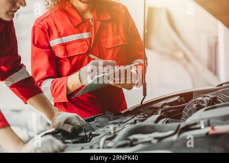 Prüfliste des Mechanikerteams Motorreparaturwartung Ölwechsel an der vorderen Motorhaube des alten Fahrzeugs in einer Werkstatt für die Kfz-Wartung Stockfoto