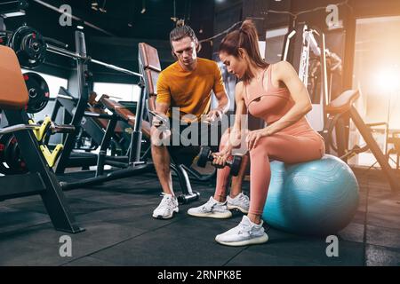 Sport-Frau trainiert Muskeln in der privaten Klasse Fitnessstudio mit Personal Trainer helfen Unterstützung Stockfoto