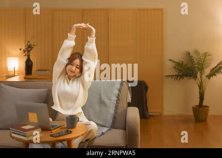 Home Lifestyle-Konzept, Junge Frau, die sich nach der Arbeit im Winter in der späten Nacht ausdehnt. Stockfoto