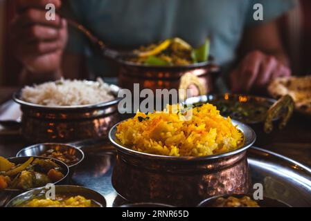 Mann, der traditionelles Essen in einem indischen Restaurant isst. Vegetarisches Thali auf dem Tablett, Hühnercurry, Reis, Naan und andere köstliche Gerichte auf dem Tisch Stockfoto