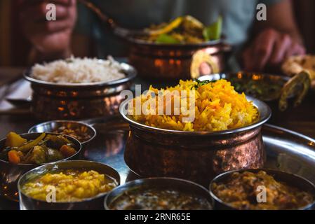 Mann, der traditionelles Essen in einem indischen Restaurant isst. Vegetarisches Thali auf dem Tablett, Hühnercurry, Reis, Naan und andere köstliche Gerichte auf dem Tisch Stockfoto