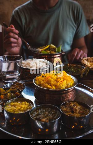 Mann, der traditionelles Essen in einem indischen Restaurant isst. Vegetarisches Thali auf dem Tablett, Hühnercurry, Reis, Naan und andere köstliche Gerichte auf dem Tisch Stockfoto