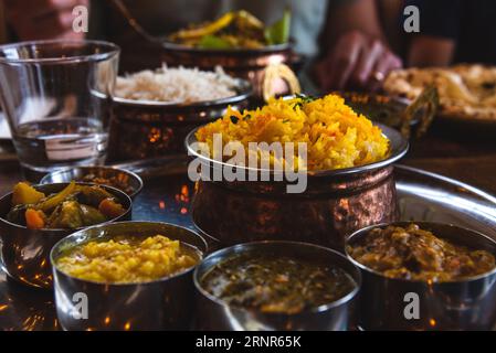 Mann isst traditionelles Essen in einem indischen Restaurant. Vegetarisches Thali auf Tablett, Hühnercurry, Reis, Naan und andere köstliche Gerichte auf dem Tisch. Stockfoto