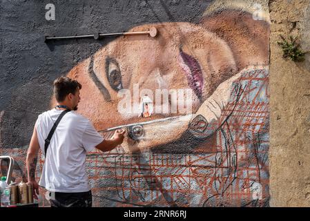 Eine Künstlerin spritzt eine weibliche Figur auf eine Hauswand als Teil des Southend City Jam Art Festivals 2023. Außerhalb der Kunstveranstaltung Stockfoto