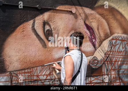 Eine Künstlerin spritzt eine weibliche Figur auf eine Hauswand als Teil des Southend City Jam Art Festivals 2023. Außerhalb der Kunstveranstaltung Stockfoto