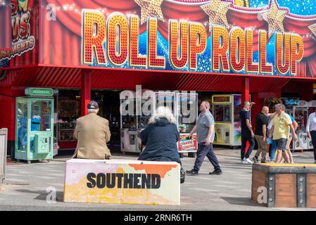 Seniorenpaar sitzt auf einem dekorierten Betonblock auf der Marine Parade außerhalb von Vergnügungsparkaden in Southend on Sea, Essex, Großbritannien, an einem warmen sonnigen Tag Stockfoto