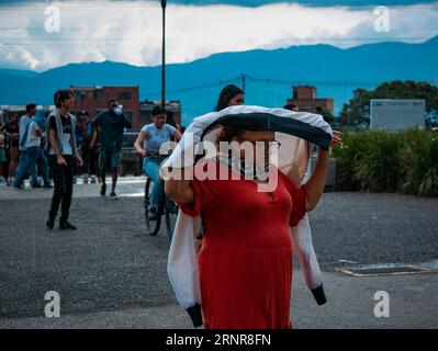 Medellín, Medellin, Antioquia, Kolumbien - Mai 28 2023: Kolumbianische Frau in roten Wanderwegen, die ihren Kopf vom Regen in einem öffentlichen Park bedeckt Stockfoto