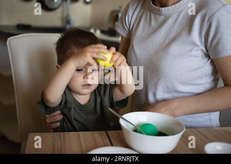 Kleiner süßer Junge mit Mutter malt Eier für ostern, die in der Küche am Tisch sitzen Stockfoto