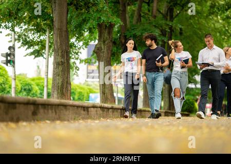 Eine große junge Gruppe von Studenten auf dem Campus, die zusammen mit Büchern und Rucksäcken zur Schule gehen Stockfoto