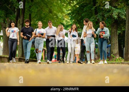 Eine große junge Gruppe von Studenten auf dem Campus, die zusammen mit Büchern und Rucksäcken zur Schule gehen Stockfoto