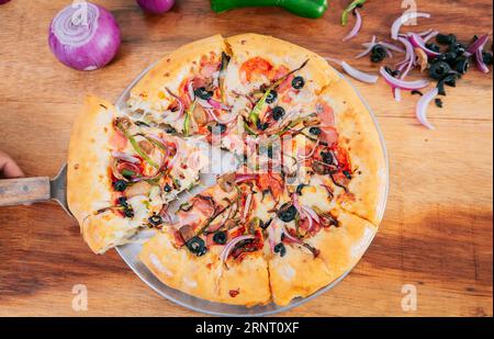 Blick von oben auf den Spatel, der ein Stück erstklassige Pizza mit Gemüse nimmt. Spatel mit einer Scheibe erstklassiger Pizza und Spatel, Blick aus dem Hochwinkel Stockfoto