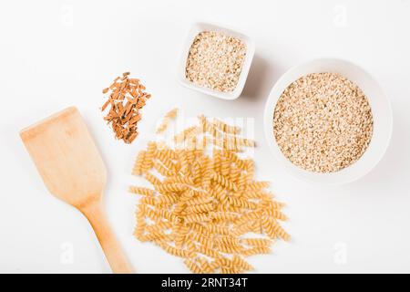 Nahaufnahme ungekochte Fusilli Pasta Reis zerkleinerter Zimt mit Spatel weißer Hintergrund Stockfoto