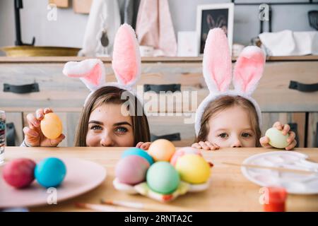 Kleine Mädchen Mutter Hasenohren versteckten Tisch mit bunten Eiern Stockfoto