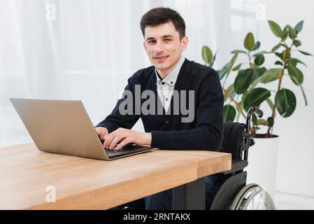 Porträt lächelnder junger Geschäftsmann im Rollstuhl mit Laptop Stockfoto