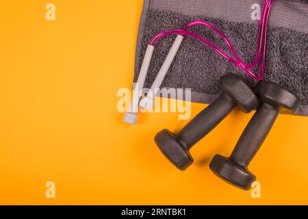 Serviette mit Draufsicht und überspringendem Seil, schwarze Kurzhanteln, gelber Hintergrund Stockfoto